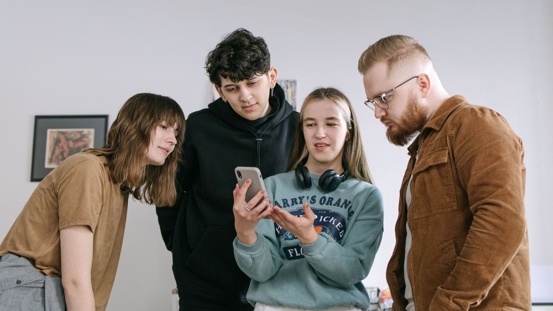 Group of young adults reviewing content on a smartphone in an office setting.