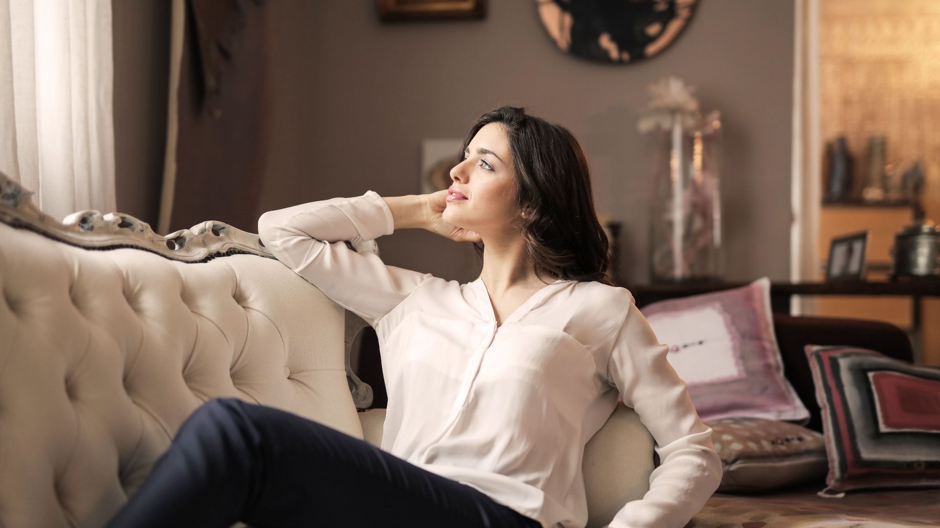 A serene woman enjoys a moment of reflection on a luxurious vintage sofa in a well-designed interior.