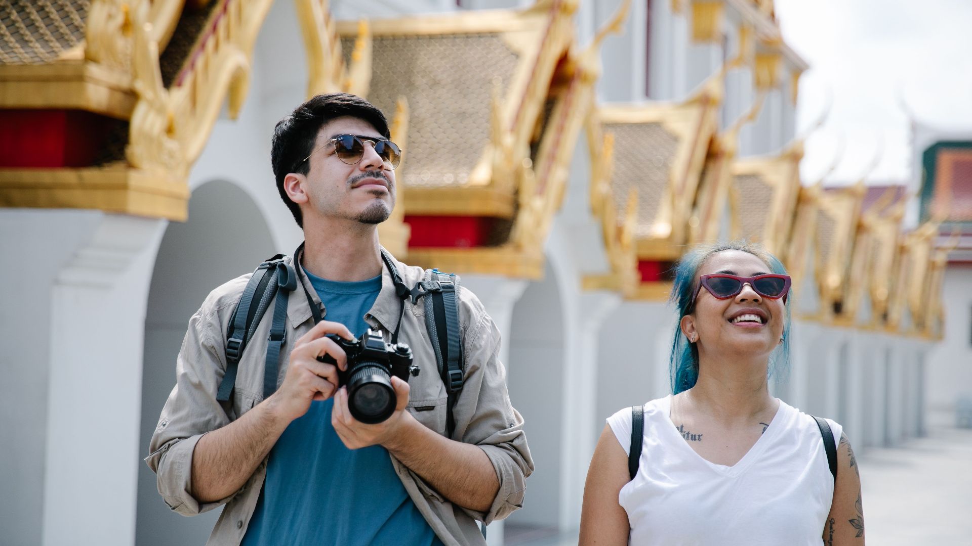 A couple explores a city's ornate architecture, capturing memories with a camera.