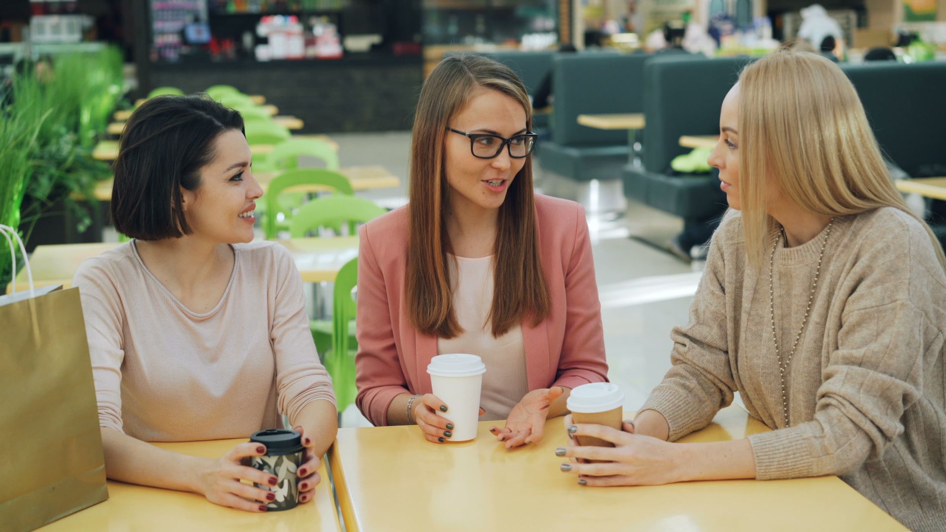 Casual conversation among friends in a modern mall cafe setting.