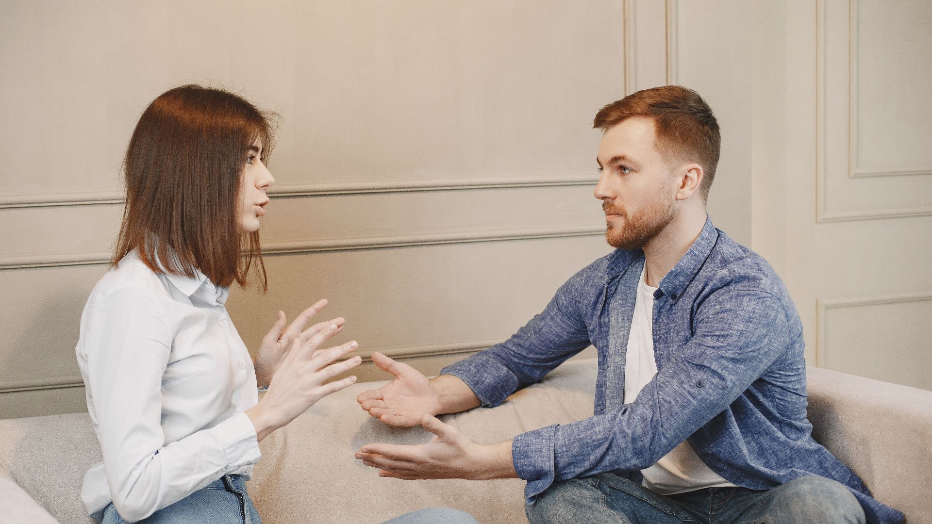 A young couple sitting on a couch having a thoughtful conversation with expressive hand gestures.