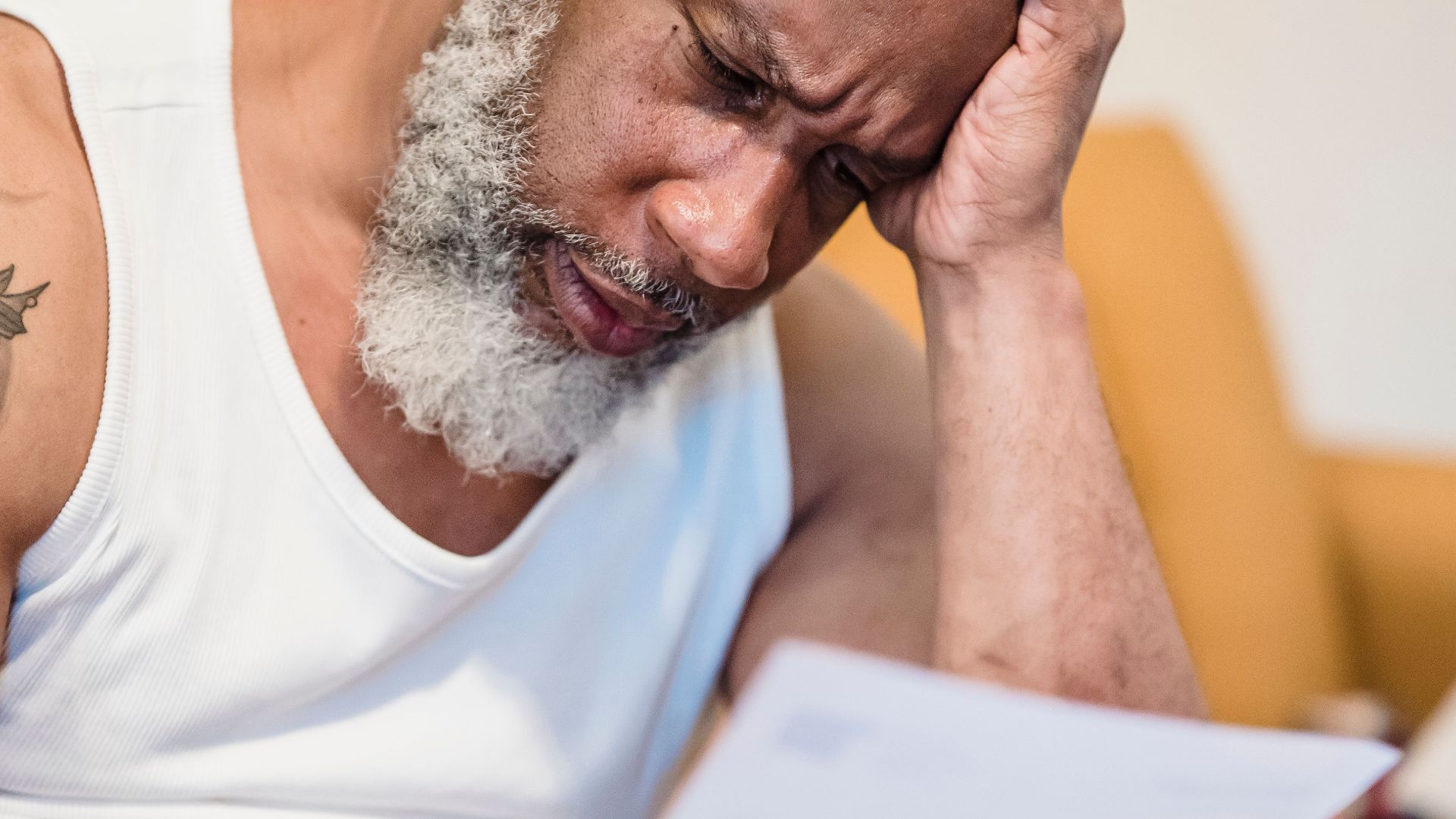 Middle-aged man in distress reading paperwork on a couch at home.