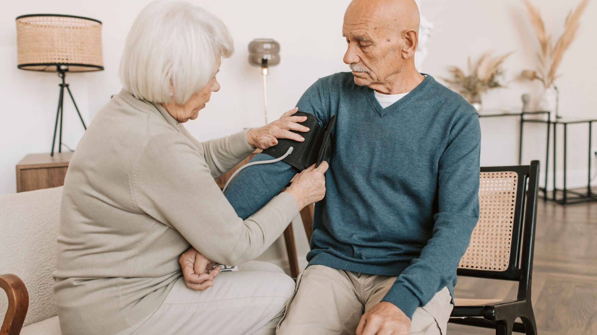 Elderly couple involved in a home blood pressure checkup, emphasizing health and care.