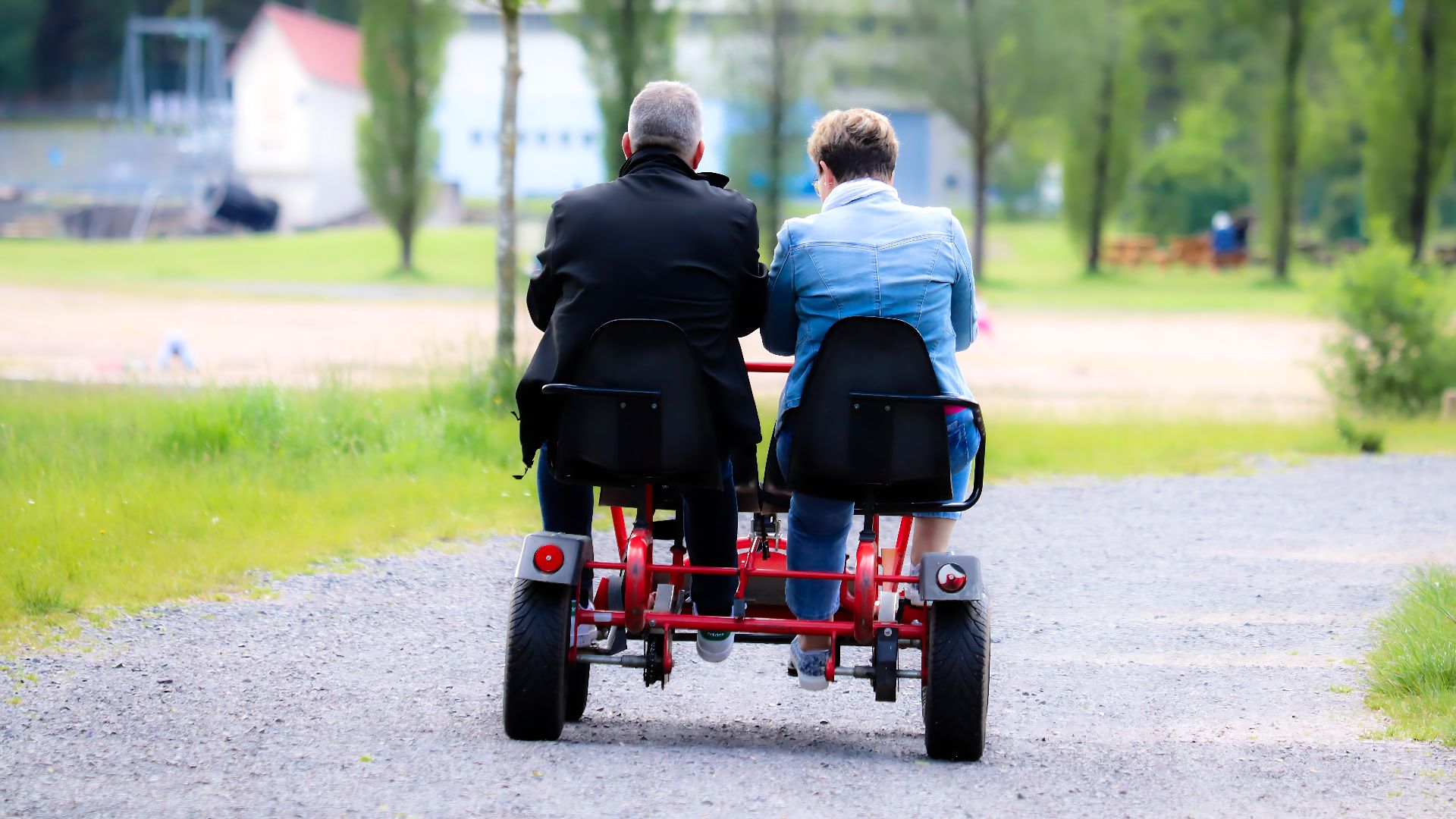 A couple enjoys a leisurely ride on a tandem bike through a lush park.