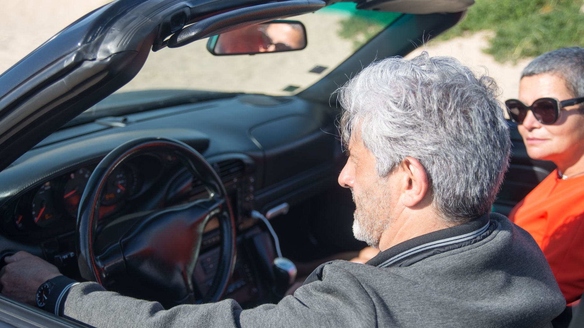 Senior couple enjoying a sunny drive in a convertible through scenic Portugal.