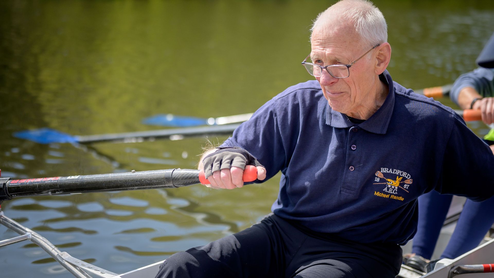 Senior man rowing a boat on a serene lake, capturing the essence of fitness and leisure.