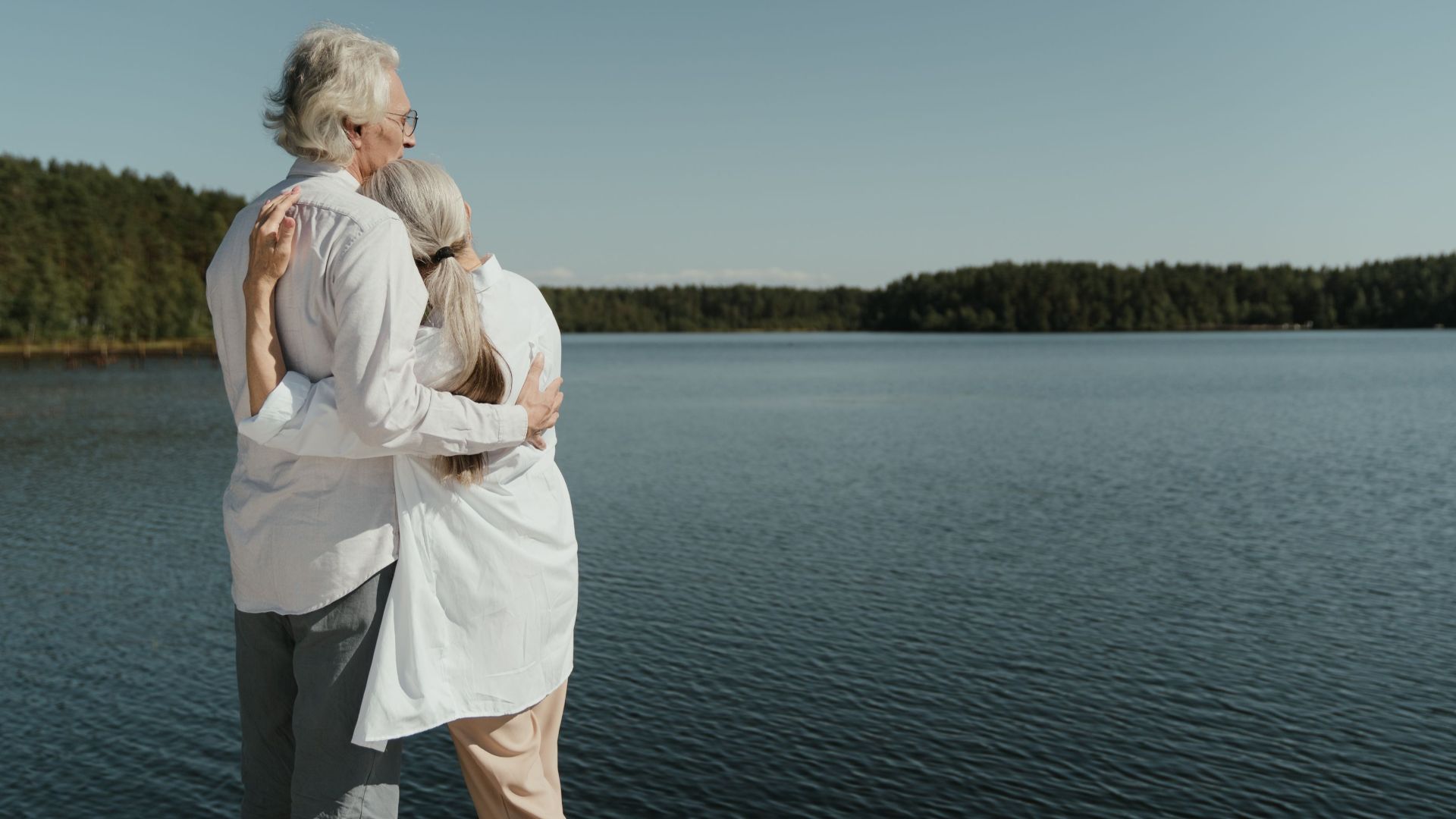 A senior couple sharing a loving embrace by a serene lakeside, symbolizing enduring love.