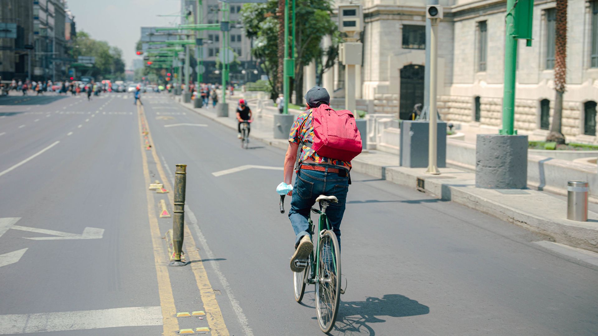 Back view of a man cycling on an empty city street on a sunny day.