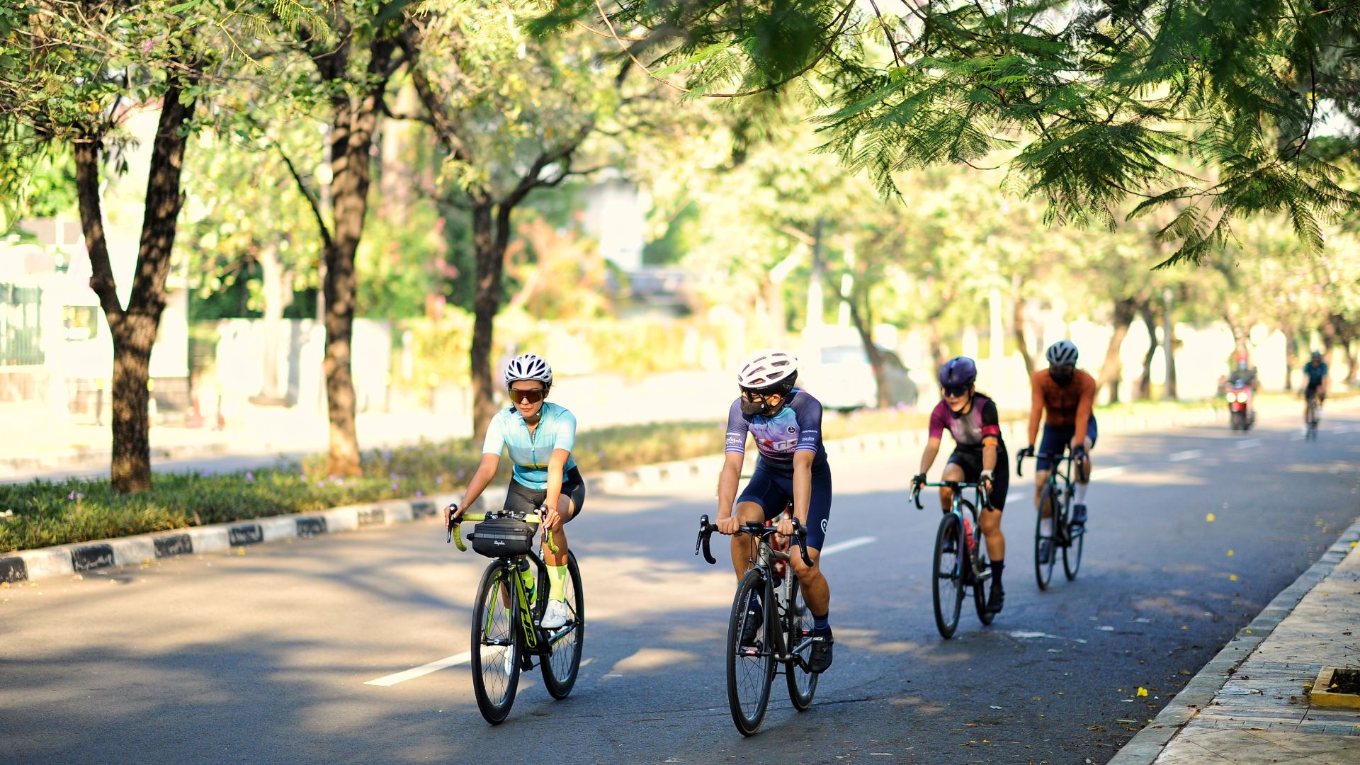 Cyclists enjoying a sunny ride through leafy roads in Jakarta, Indonesia.