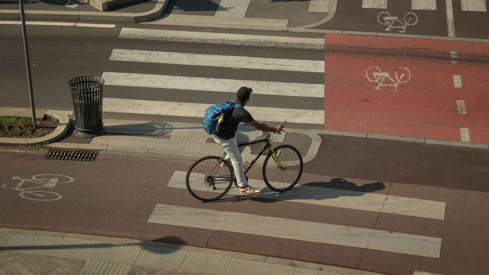 A cyclist with a backpack rides across a zebra crossing in a city intersection with bike lanes.
