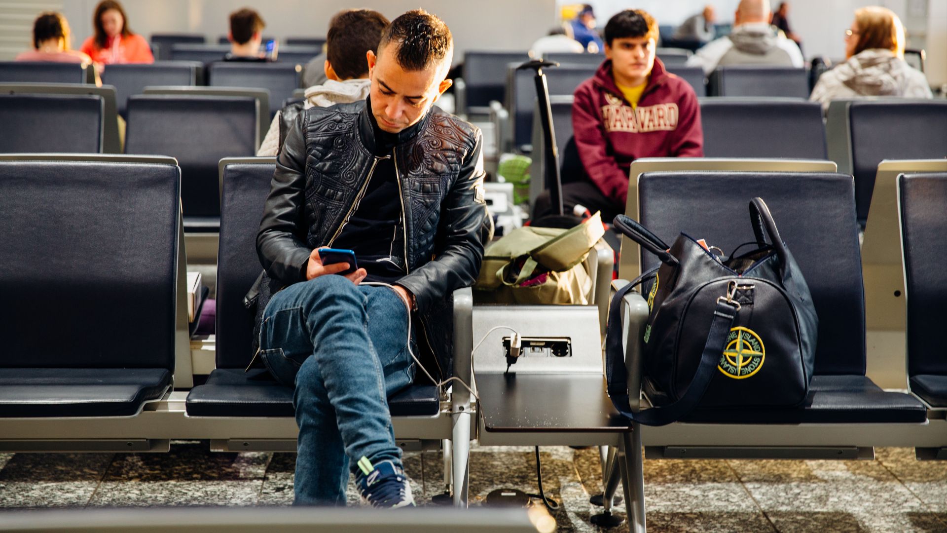 People sitting in an airport lounge, focused on smartphones and waiting for flights.