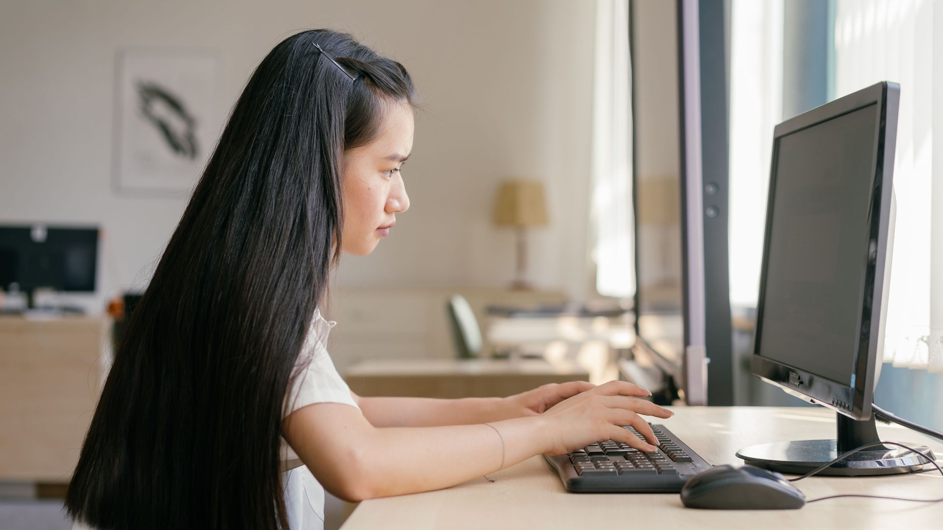 A young woman working intently on a computer in a bright, modern office setting, embodying productivity.