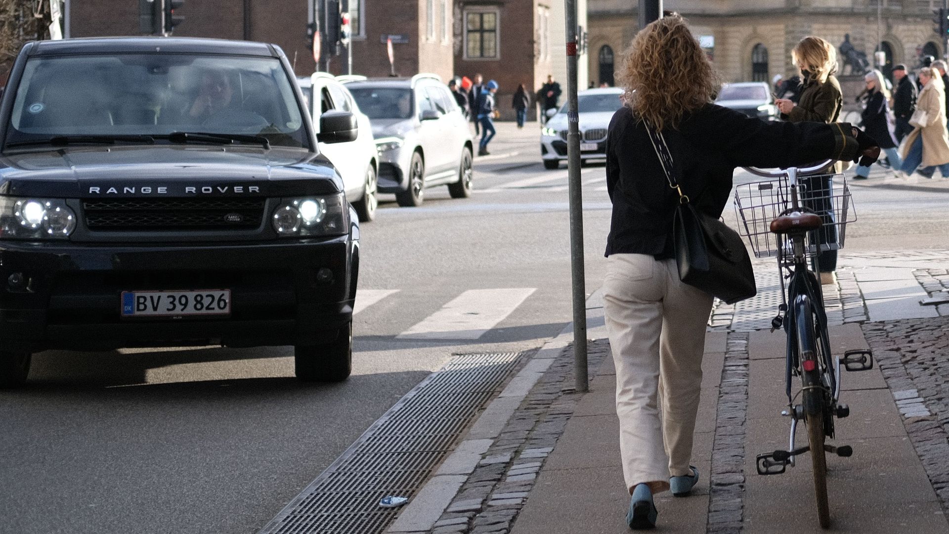Street scene in Copenhagen with a woman walking her bicycle, showcasing urban life and architecture.