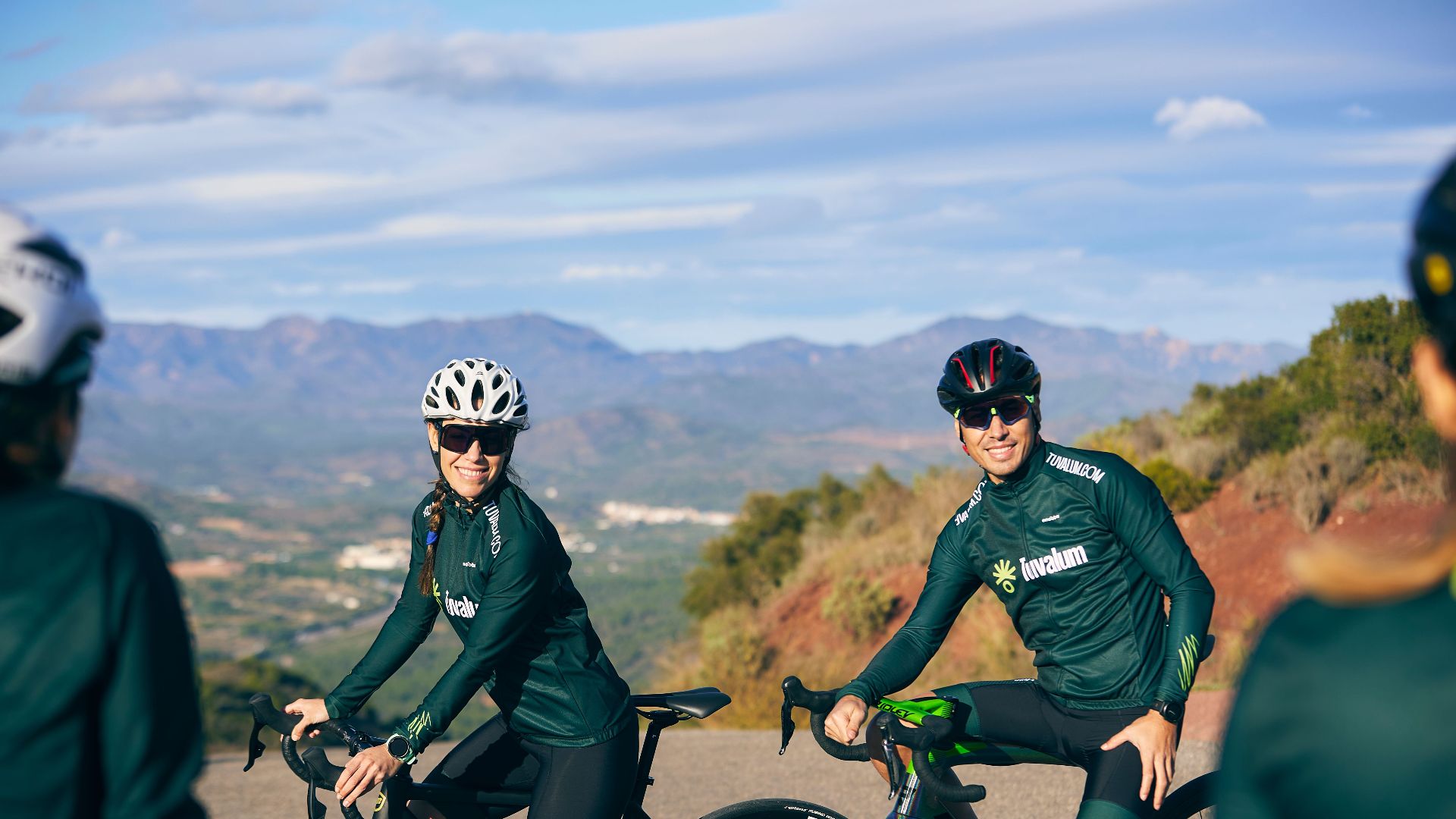 Group of cyclists enjoying a scenic ride on a mountain road, wearing sportswear and helmets.