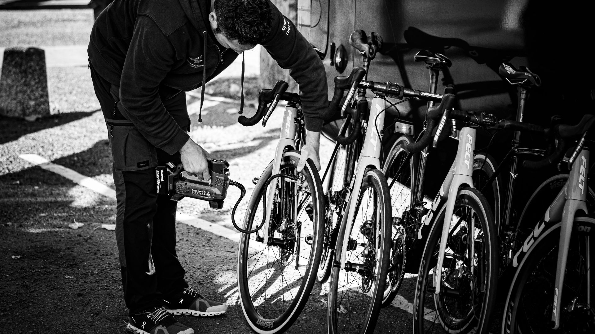 A man in a hoodie examining a row of road bicycles outdoors.