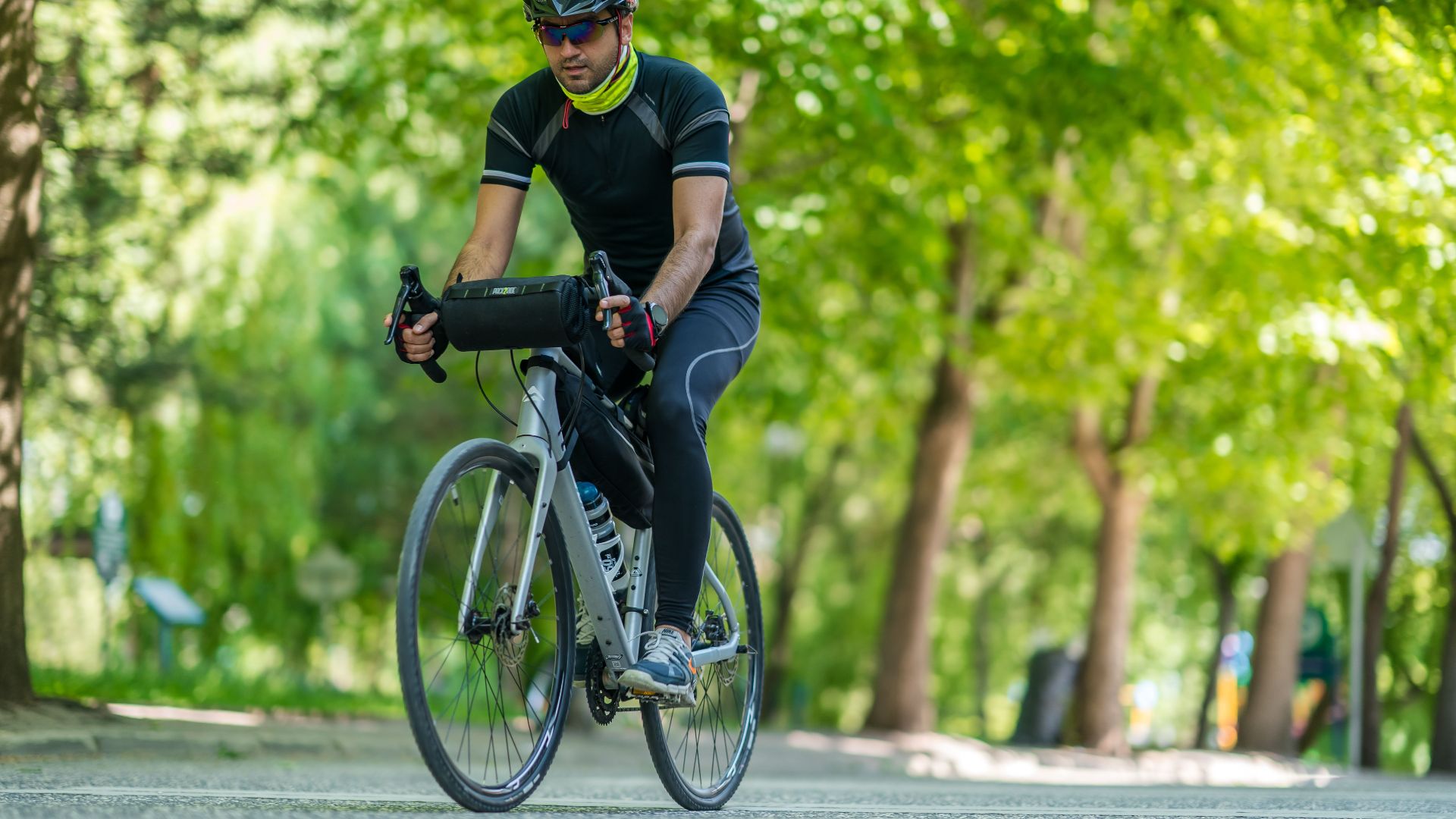 Man cycling on a sunny day in a lush green park, wearing active wear and helmet.