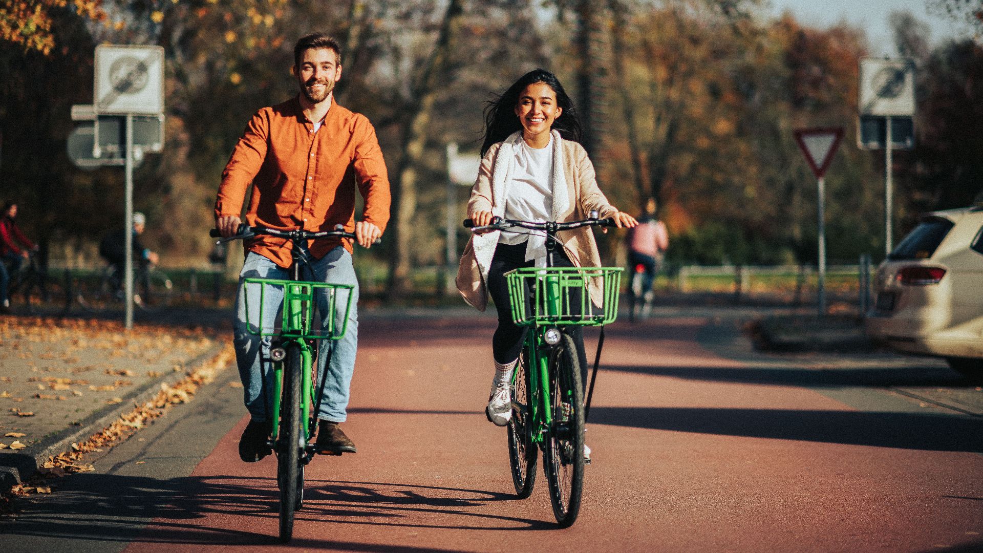 Man and woman riding bicycles on a sunny autumn street in a park.