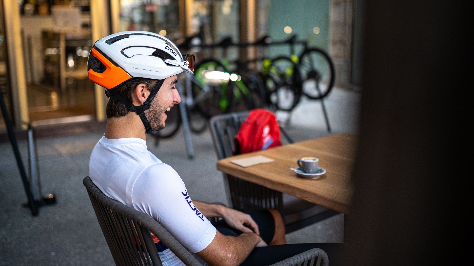 A cyclist resting at a cafe, enjoying a cup of coffee, wearing a helmet and cycling gear.