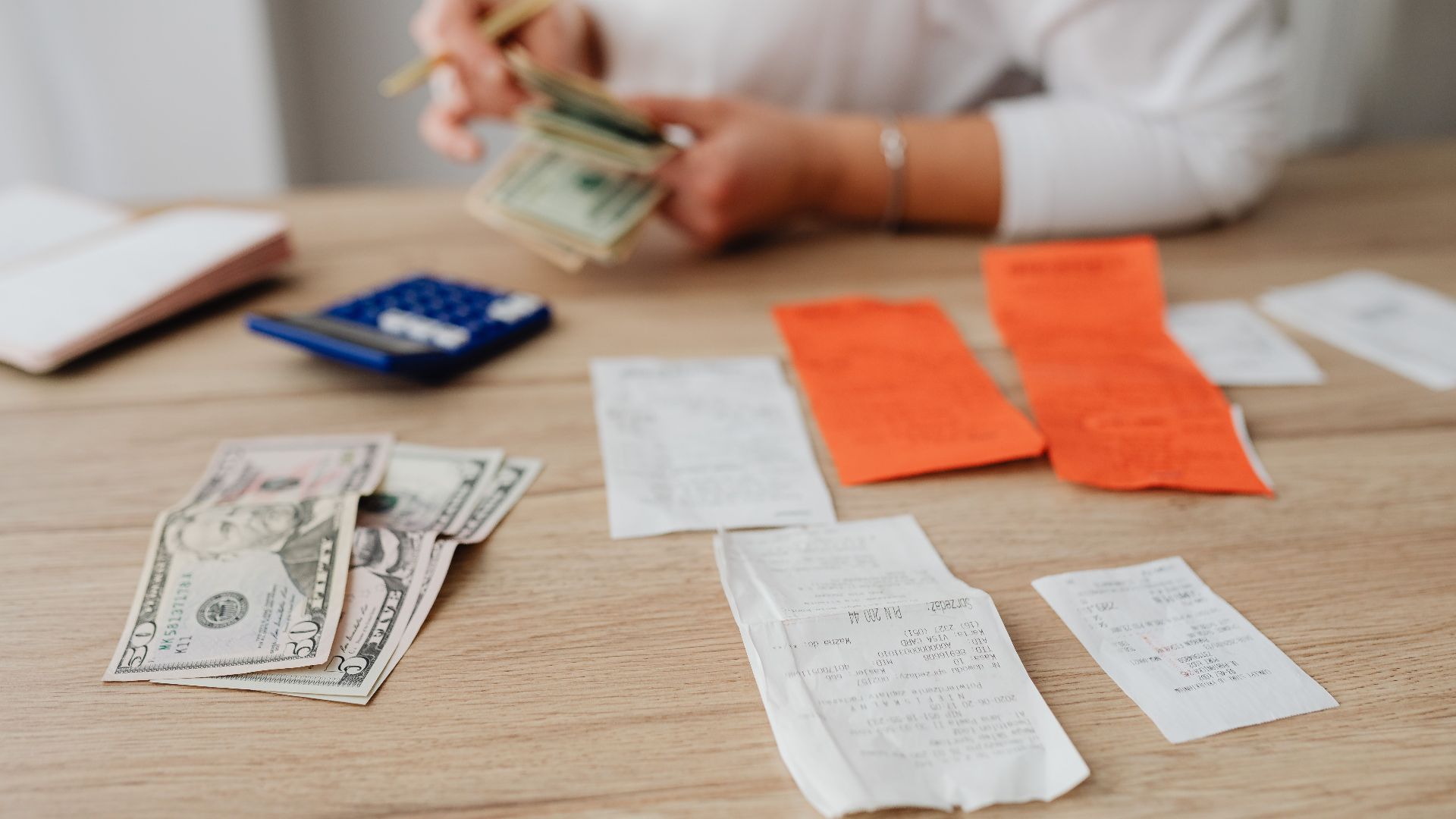 A person using a calculator and cash to plan a household budget.