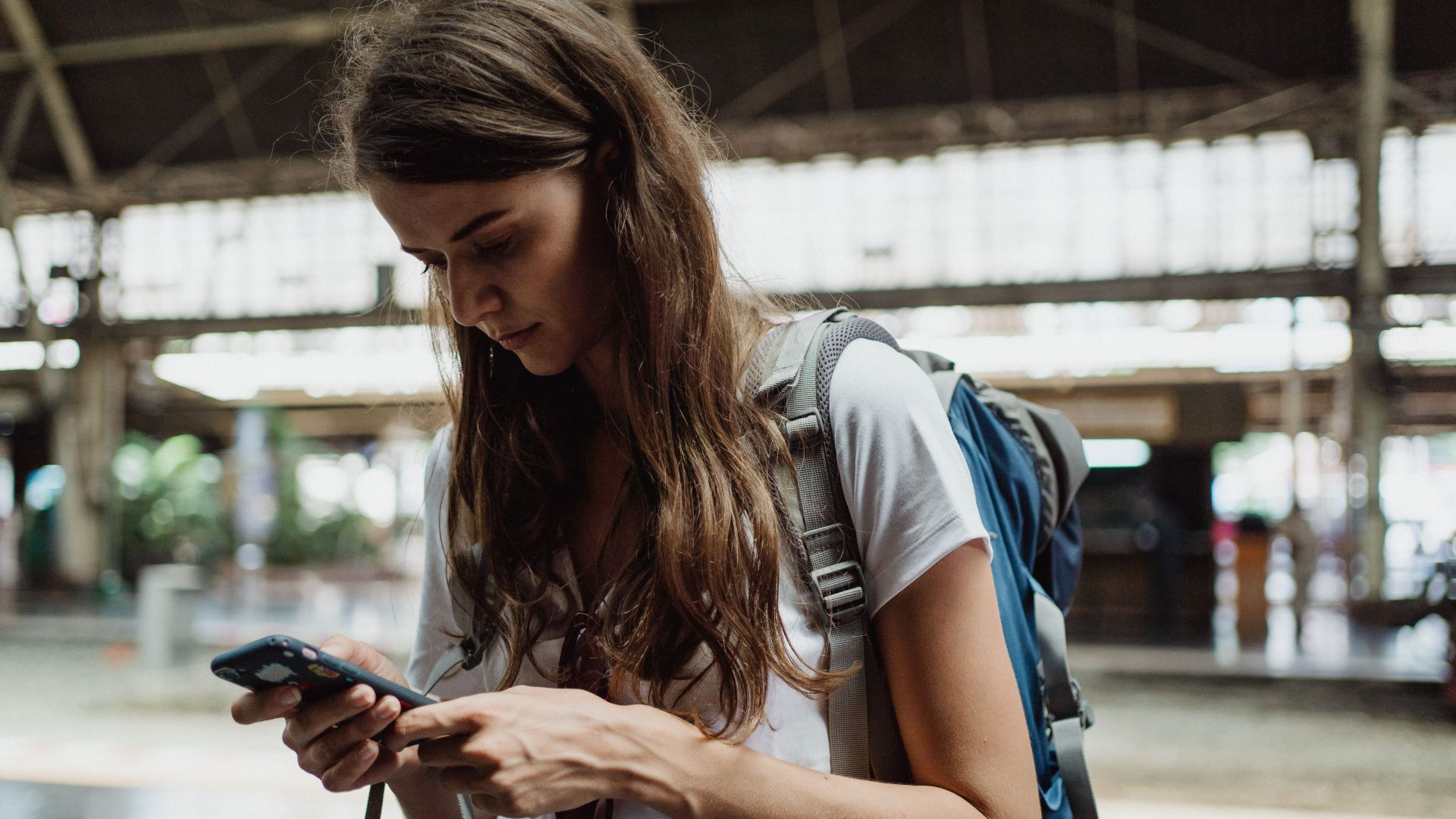 A young woman checks her smartphone while traveling at a train station.
