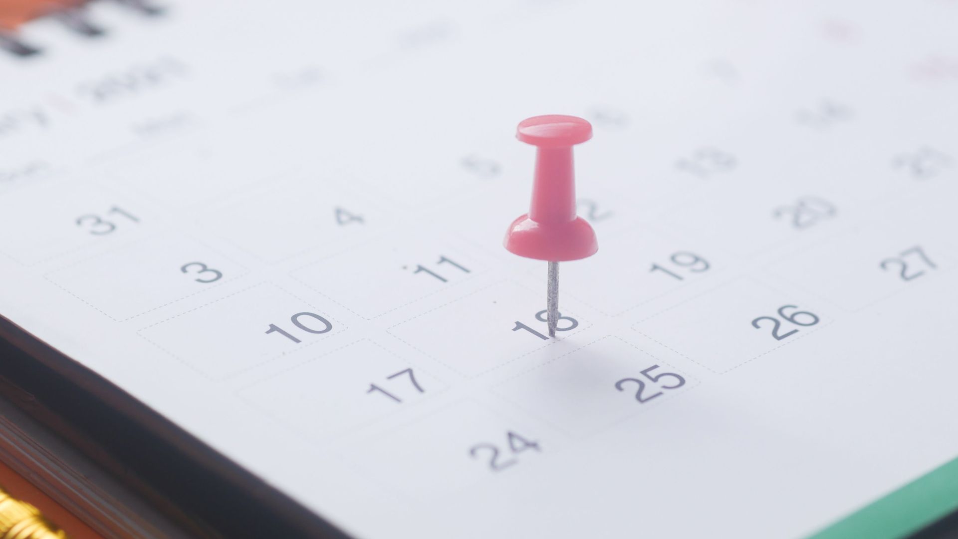 A close-up of a calendar page with a pink push pin, pencil, and binder clip on an orange background.