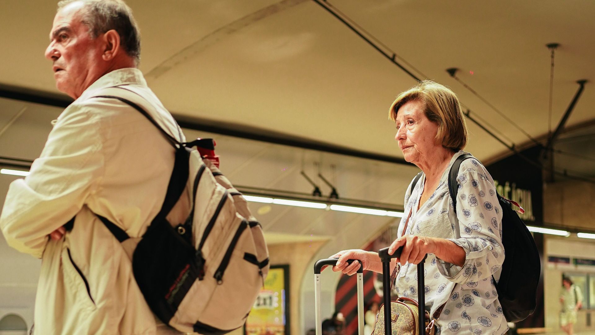 Elderly couple with luggage at a Lisbon subway platform, poised for travel adventure.