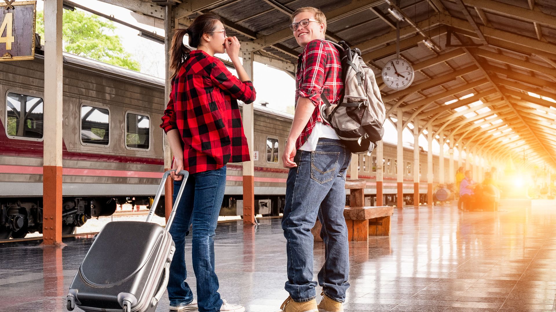 Young couple in a railway station, ready for travel. Bright morning scene with backpacks and luggage.