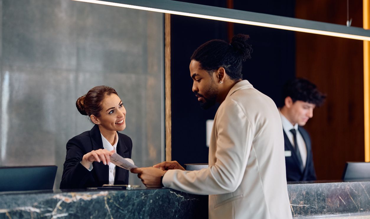 Shutterstock-2434774073, African American man registering in a hotel with assistance of front desk receptionist.