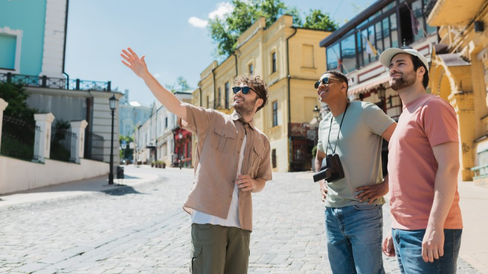 Tour guide in sunglasses pointing with hand during excursion with interracial tourists.  The photo depicts an outdoor concept of work, suggesting a flexible and mobile approach to professional tasks.
