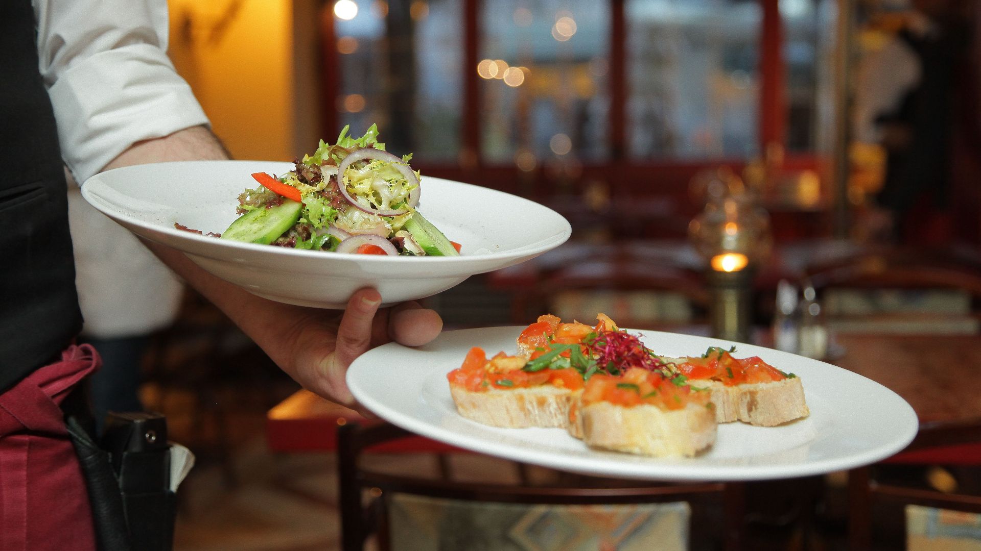 A waiter serves a fresh salad and hors d'oeuvres in a cozy restaurant setting.