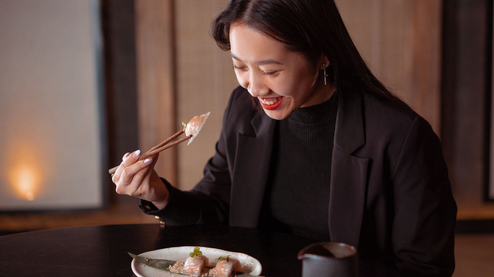 Asian woman happily dining on dumplings using chopsticks in a warm indoor setting.