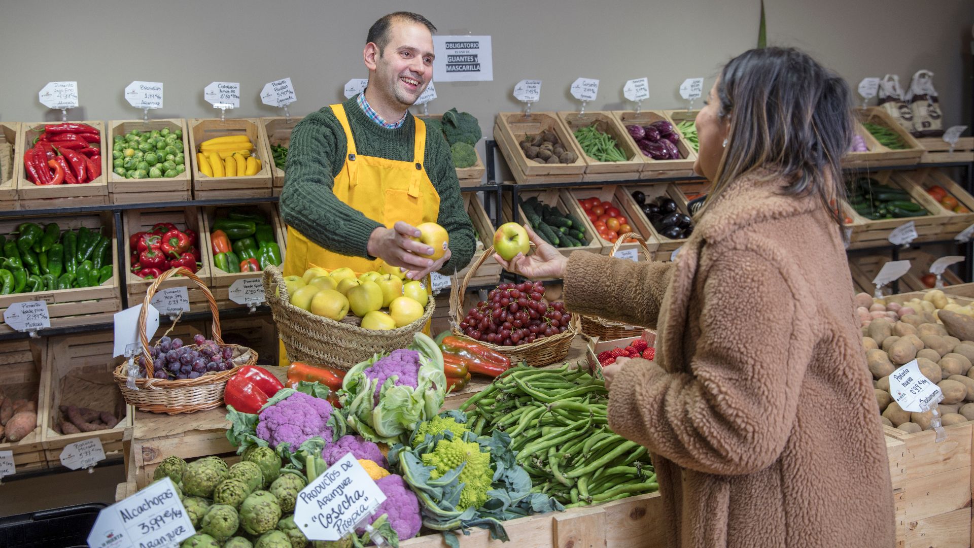 Man in yellow apron and woman exchanging fresh fruits at a vibrant market in Madrid.