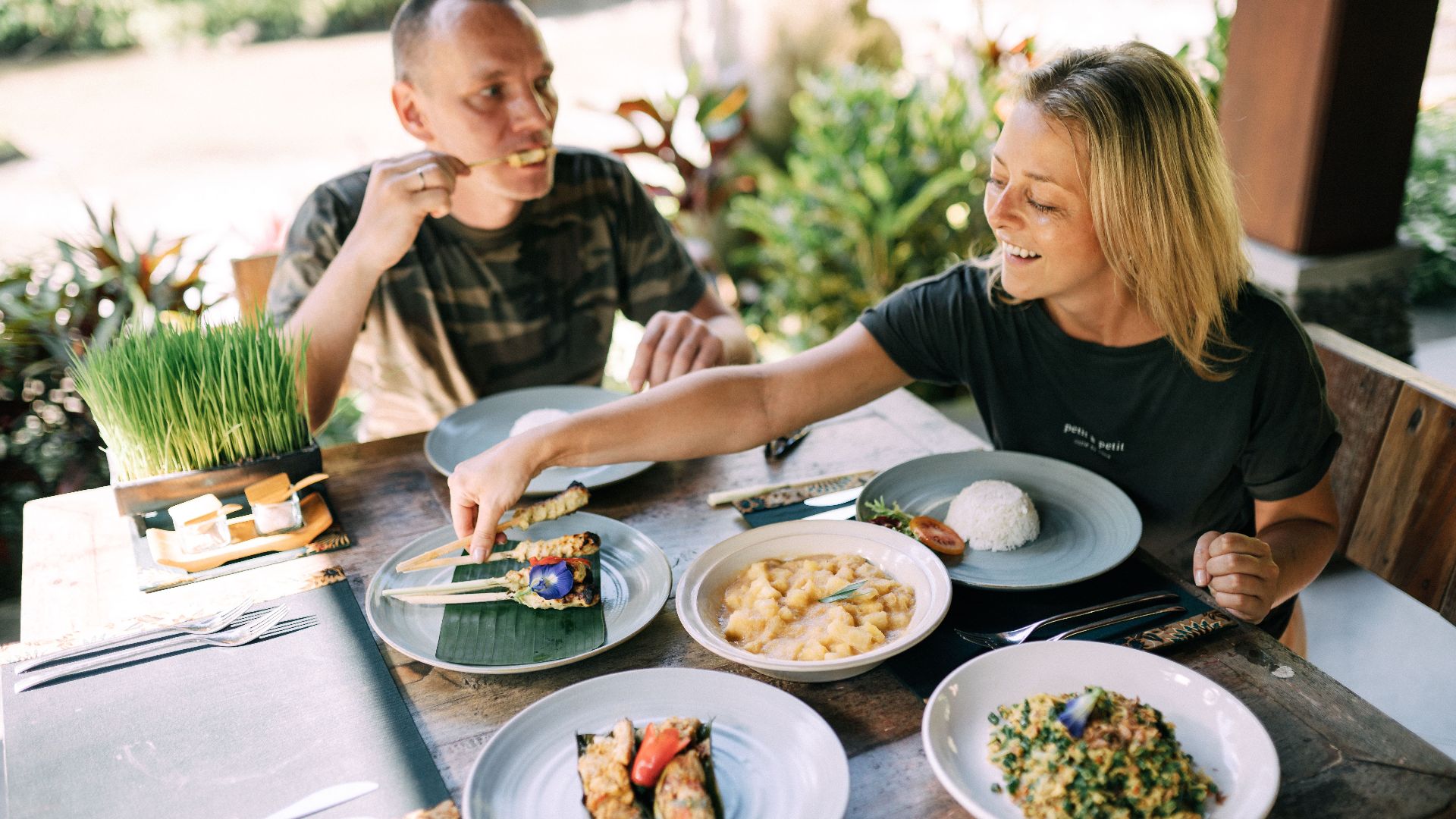 A couple enjoying a variety of Asian dishes outdoors at a cozy table setting.