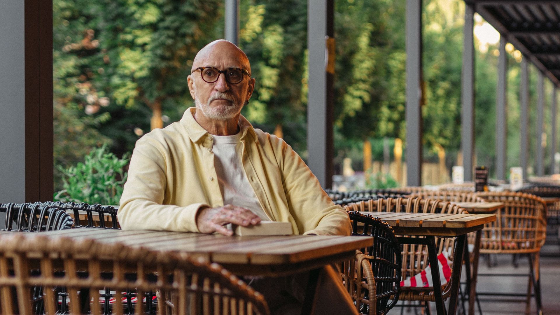 Senior man sitting alone at an outdoor café patio during summer evening.