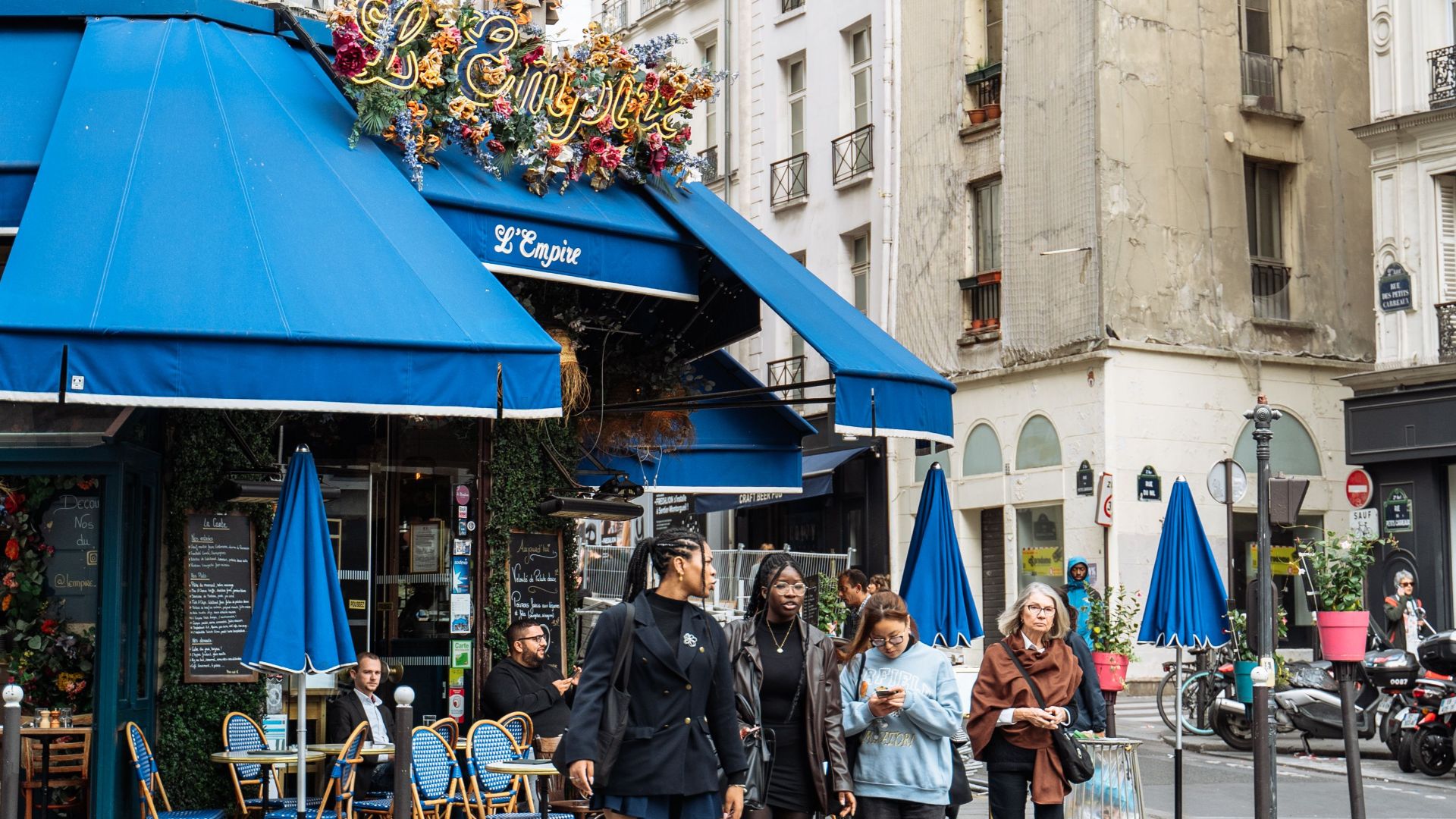 Charming view of a Parisian cafe with pedestrians crossing on a lively Paris street.