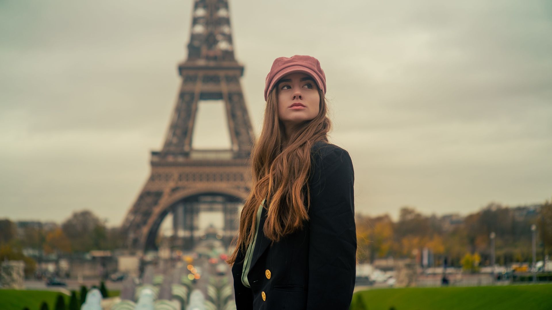 A young woman stands elegantly in a Paris park with the Eiffel Tower in the background, embracing the fall ambiance.