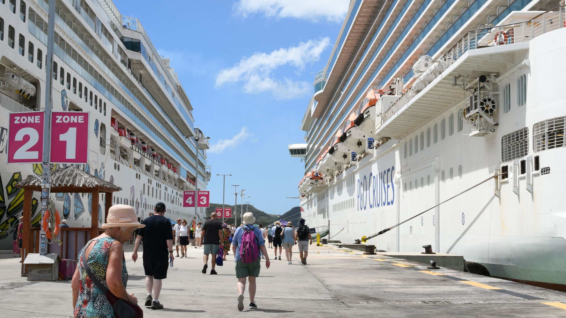Bustling cruise port with tourists, featuring two large cruise ships under a bright blue sky.