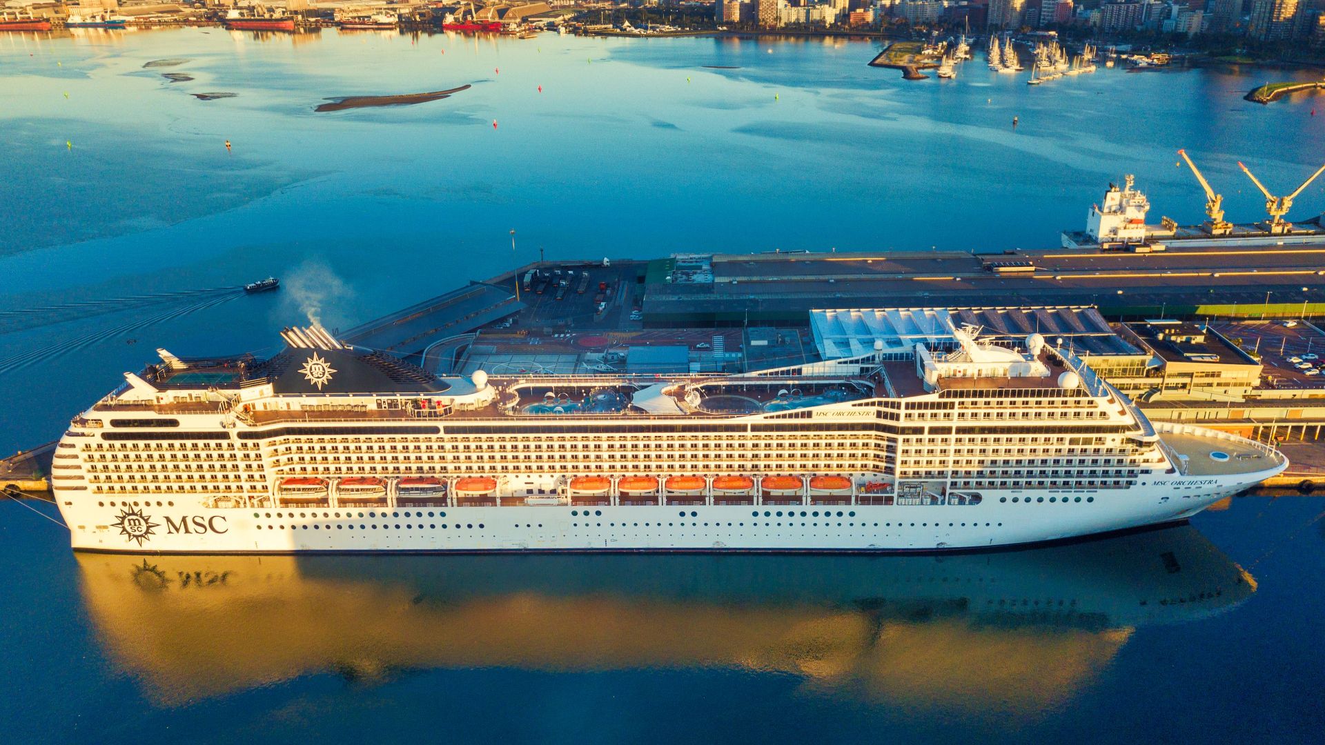 Aerial view of a cruise ship docked at a South African harbor with city skyline.