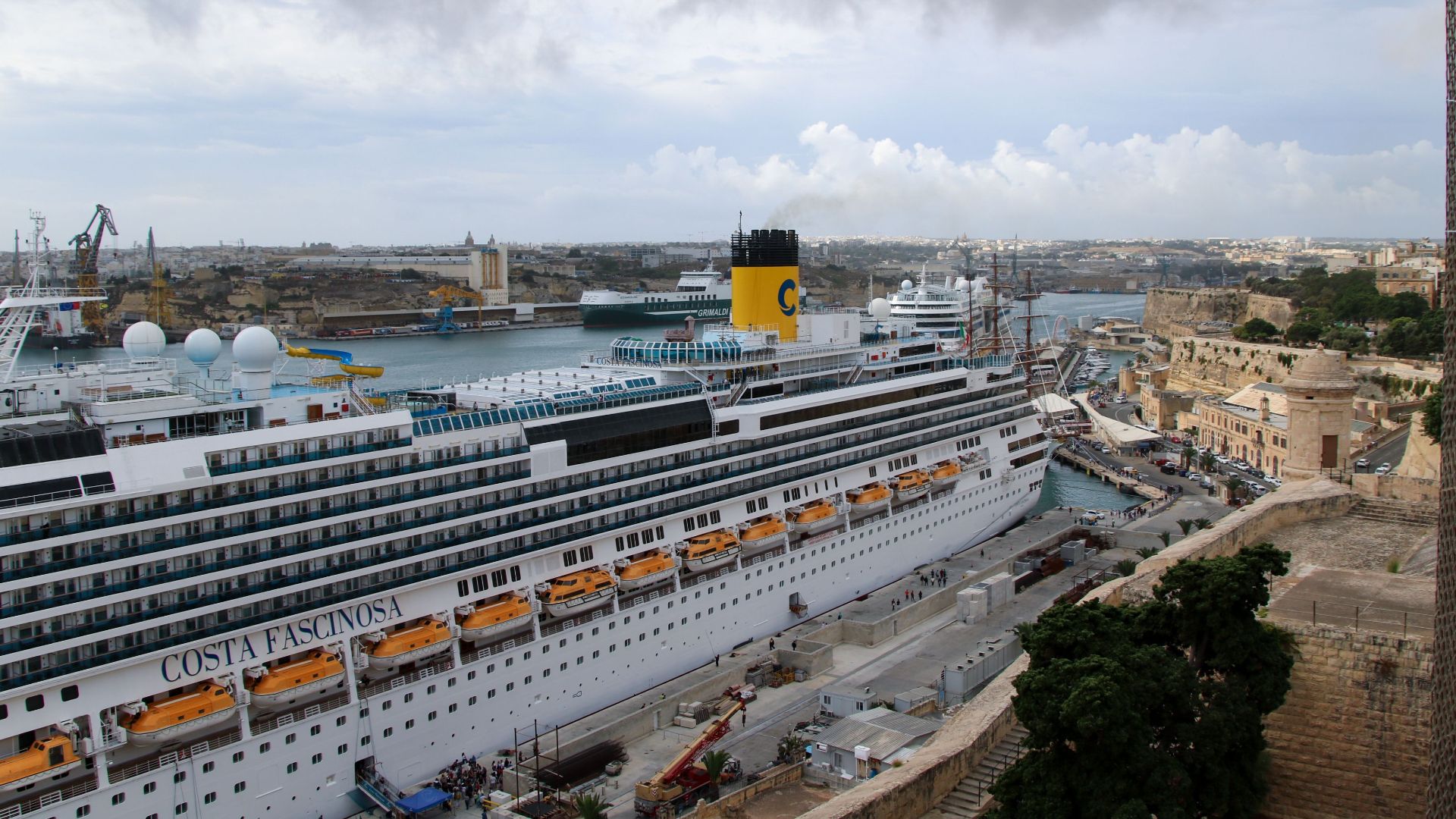 Aerial view of a large cruise ship docked at La Valletta port, Malta, with overcast skies.