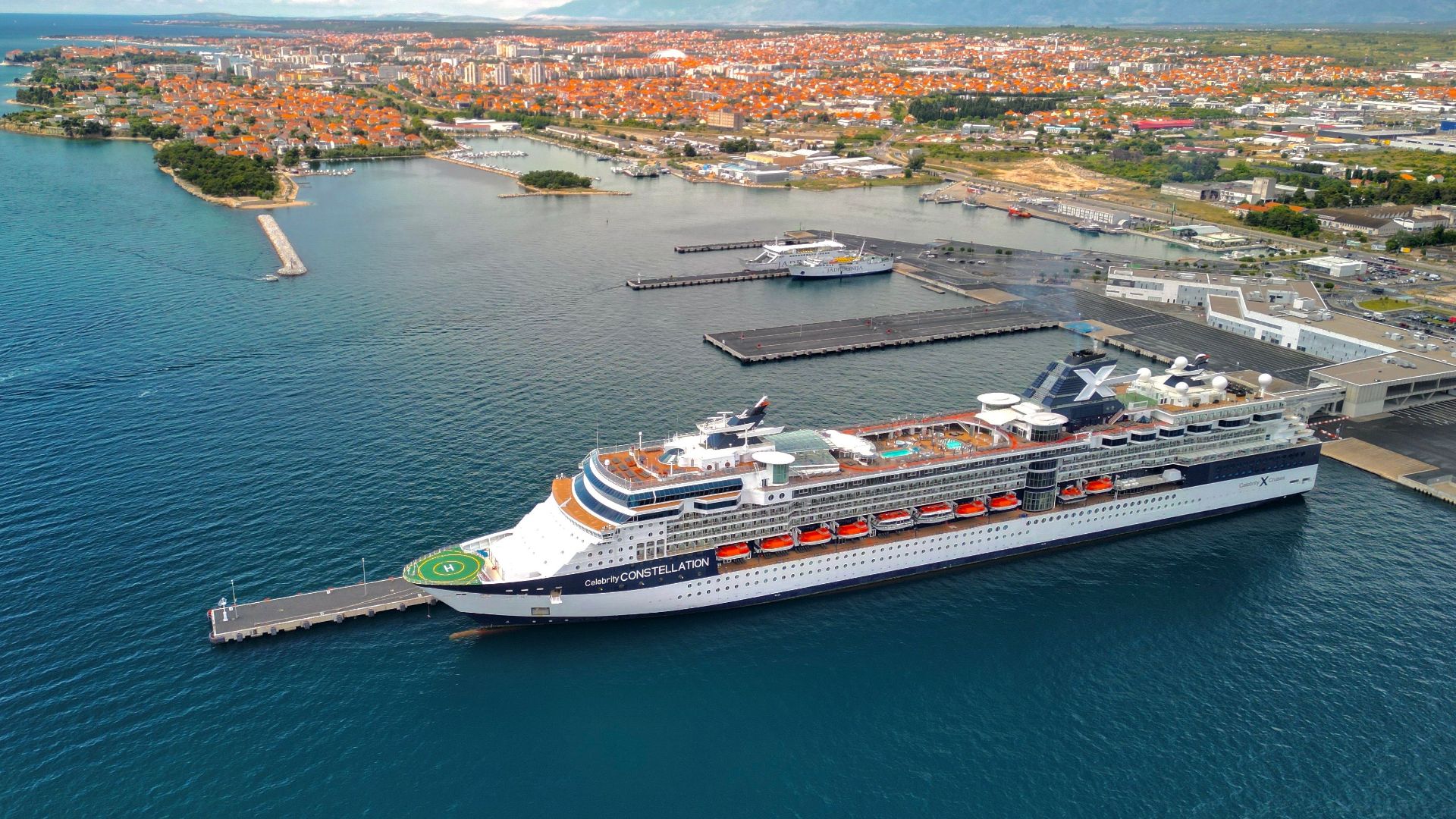Explore a stunning aerial shot of a cruise ship at a bustling harbor with a vibrant coastal city backdrop.