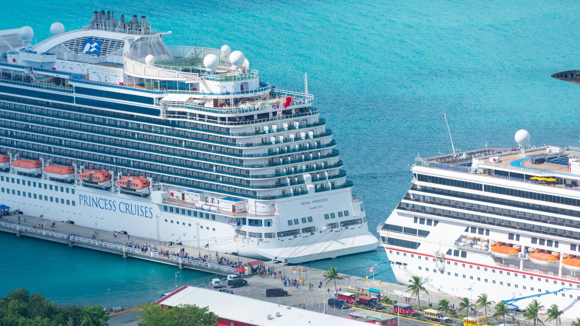 Aerial view of grand cruise ships docked at a tropical pier with turquoise waters.