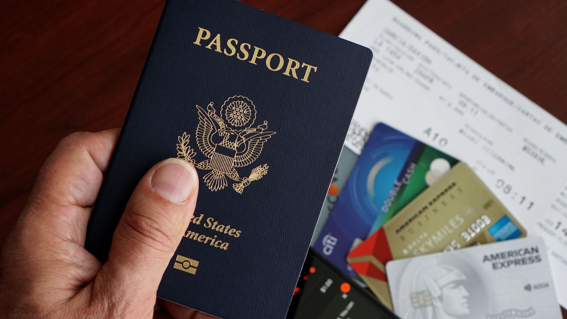 A close-up of a US passport with credit cards, tickets, and a mobile phone on a table.