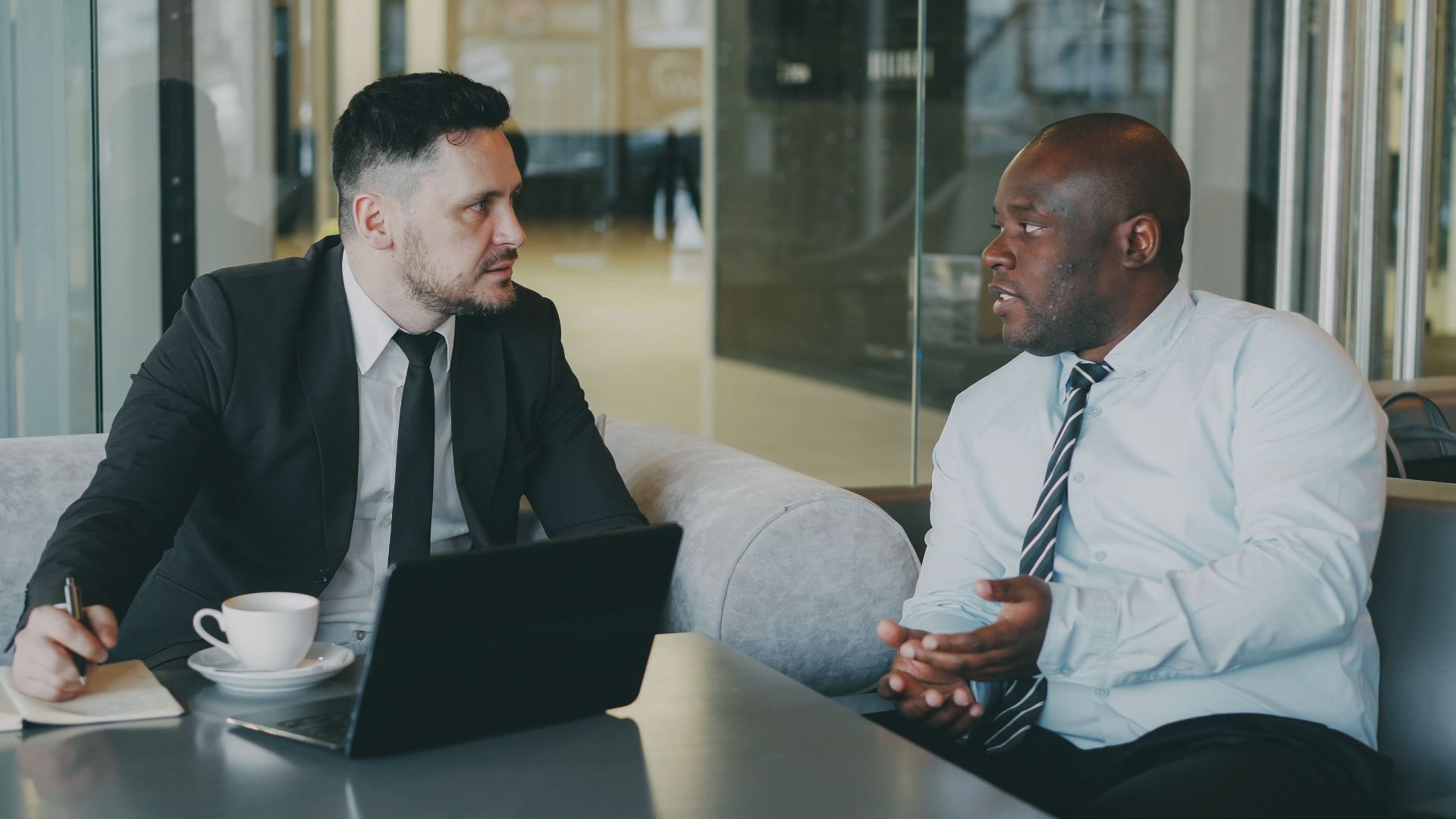 Two businessmen discussing at a cafe with a laptop and coffee.