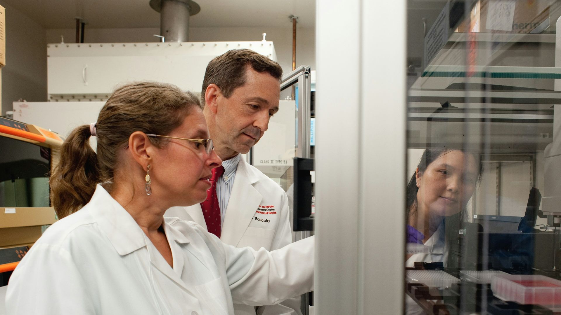 a man and a woman in lab coats looking at something in a cabinet