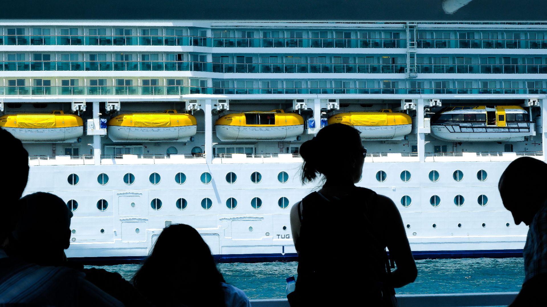 Silhouettes of people observing a large cruise ship from a dock in Türkiye.