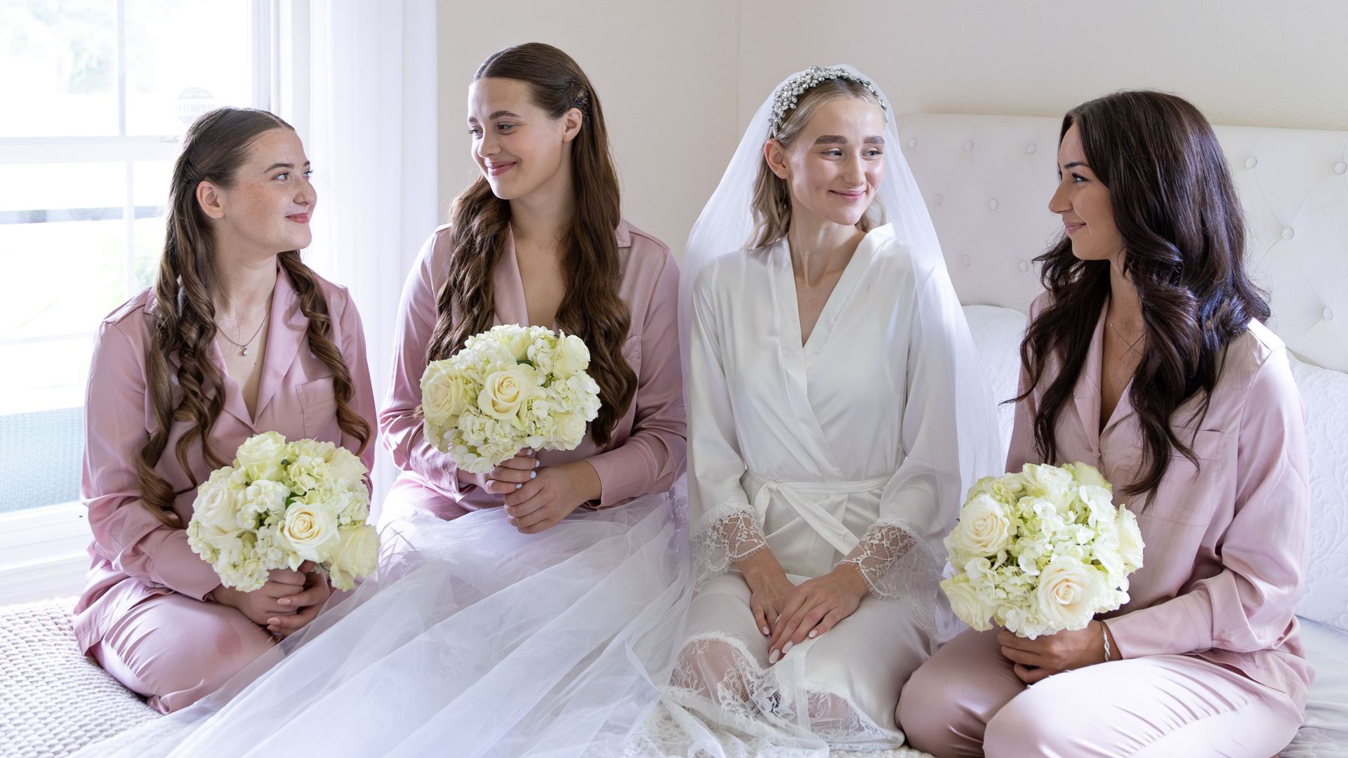 Bride and bridesmaids sharing a joyful moment in matching pink pajamas before the wedding ceremony.