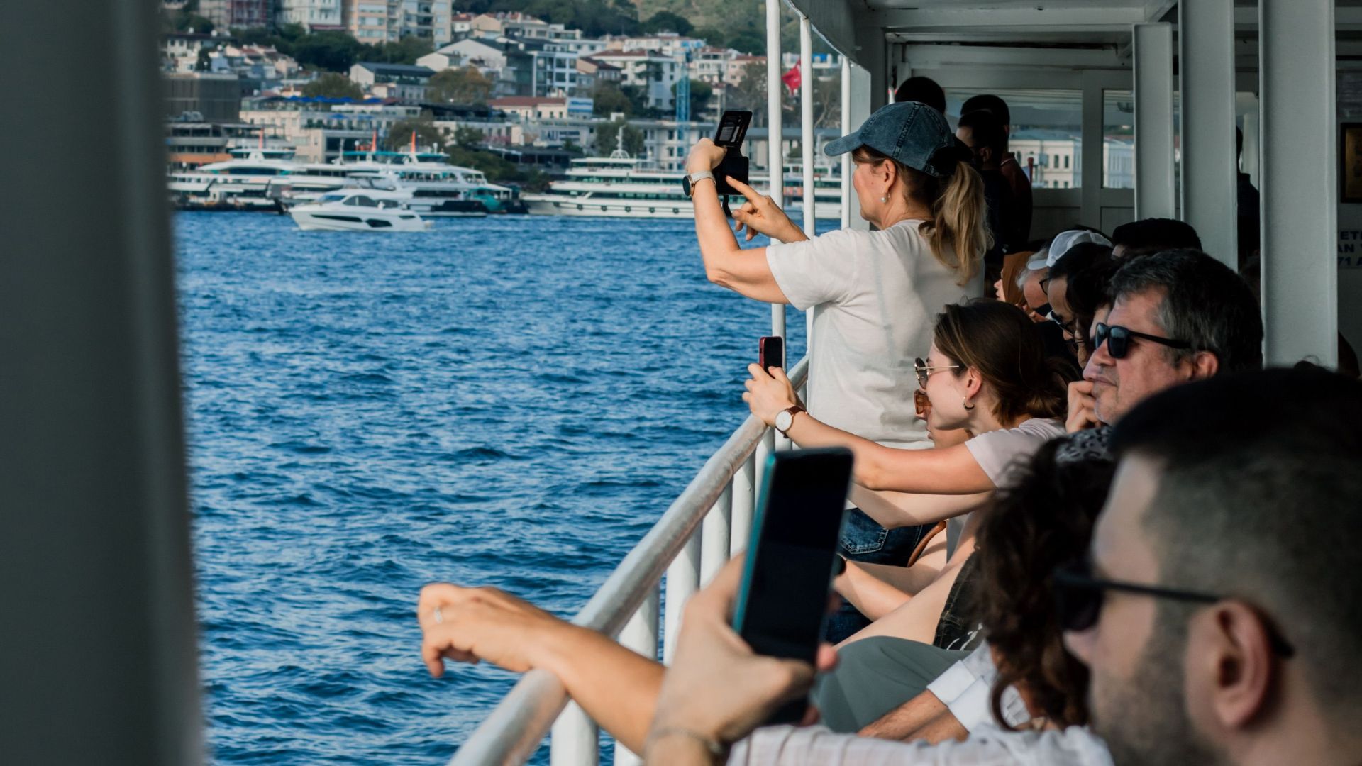 Group of tourists capturing scenic views from a ferry's deck on a sunny day.