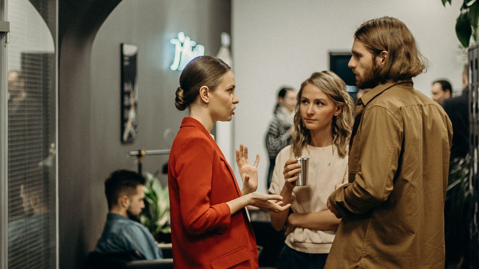 A lively casual office gathering with people engaged in conversation in a modern indoor setting.