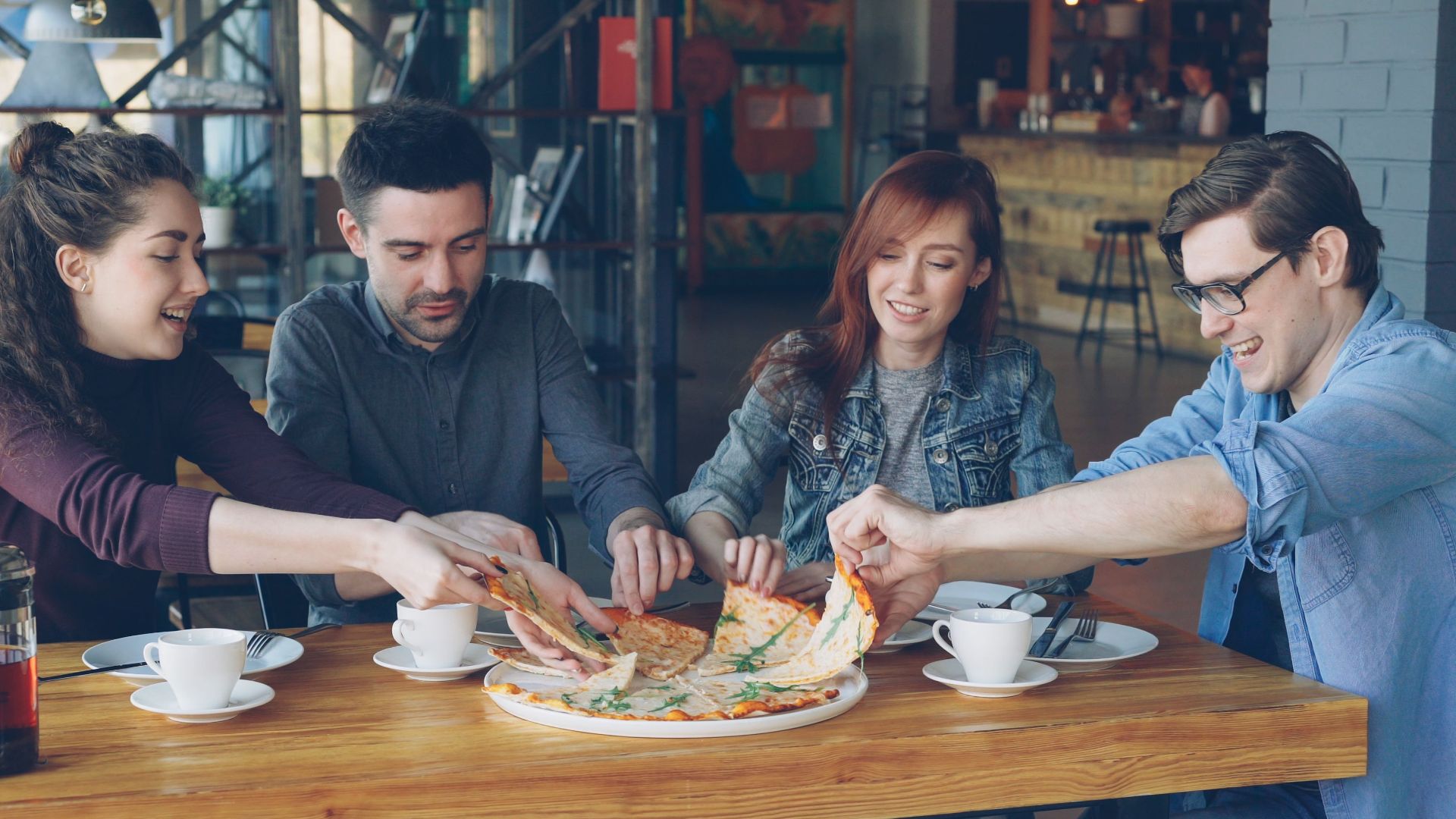 A group of friends enjoying pizza and coffee in a casual cafe setting.