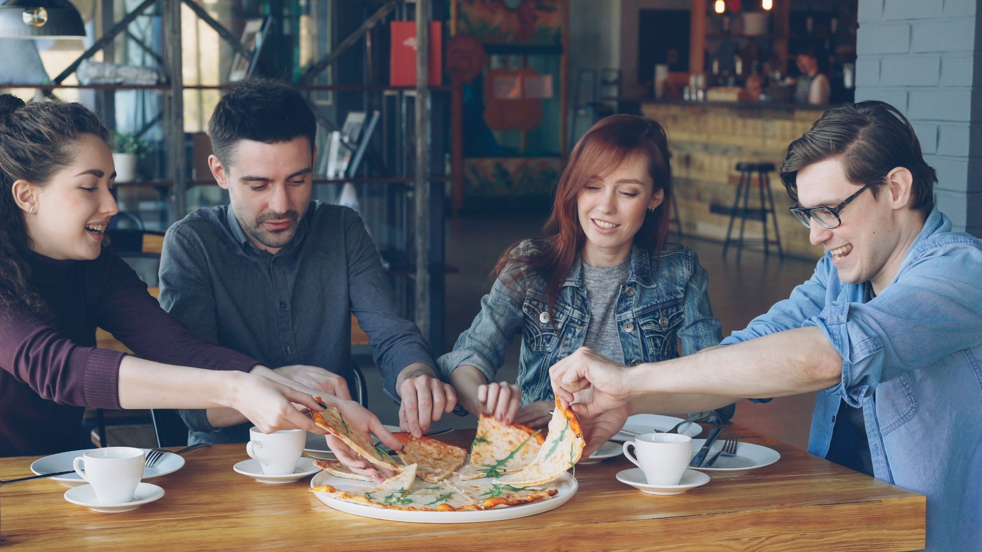 A group of friends enjoying pizza and coffee in a casual café setting.